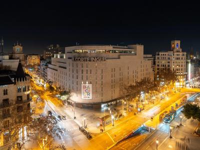 A night-time long-exposure photograph of a busy urban intersection featuring a large building with "EL CORTE INGLES" signage, light trails from traffic, and surrounding city architecture.