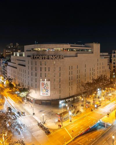 A night-time long-exposure photograph of a busy urban intersection featuring a large building with "EL CORTE INGLES" signage, light trails from traffic, and surrounding city architecture.