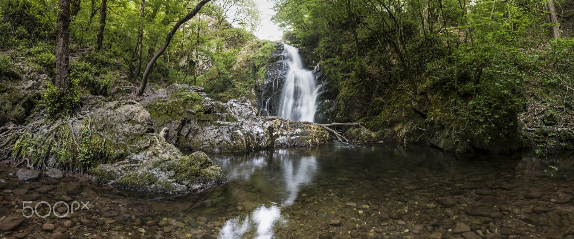 The image shows a waterfall cascading into a pool within a forest, with a "500px" watermark in the bottom left corner.