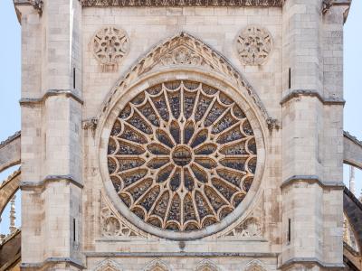 A close-up view of a large Gothic rose window set within the light-colored stone facade of a cathedral, flanked by flying buttresses.