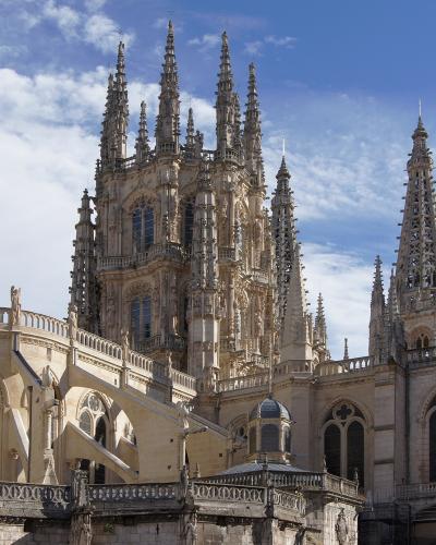The image shows the ornate Gothic spires and flying buttresses of a large cathedral against a blue sky with clouds.
