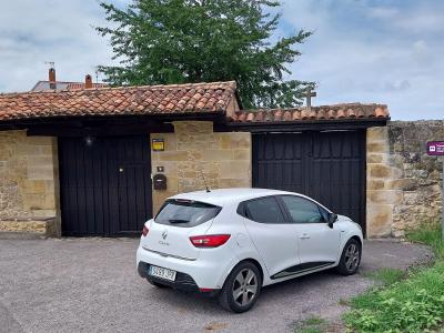 A white Renault Clio is parked in front of a stone building with black wooden gates and a terracotta tiled roof, next to a purple signpost.