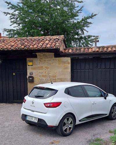 A white Renault Clio is parked in front of a stone building with black wooden gates and a terracotta tiled roof, next to a purple signpost.