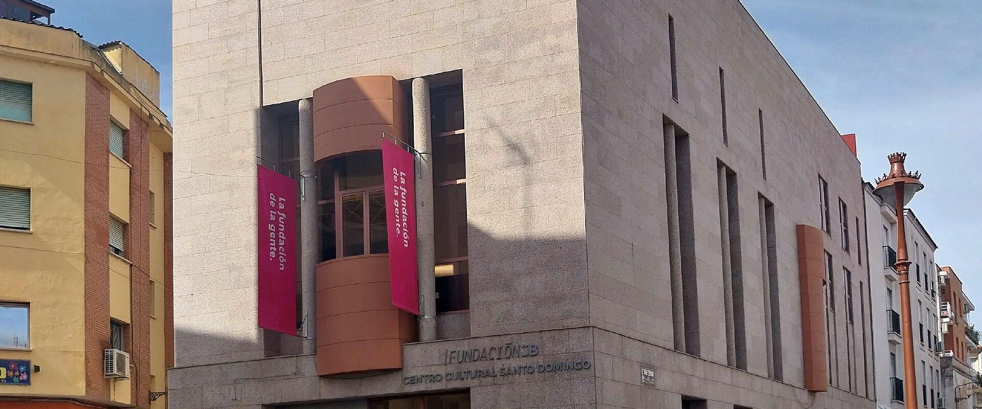 A modern, light-colored stone building with vertical slit windows and pink banners hanging from a curved balcony section.