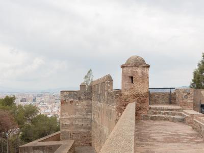 A view from the ramparts of a historic stone fortress featuring a brick sentry box (garita) overlooking a dense coastal city and sea.