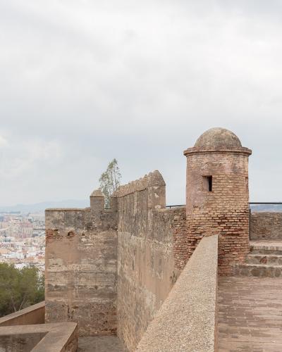 A view from the ramparts of a historic stone fortress featuring a brick sentry box (garita) overlooking a dense coastal city and sea.