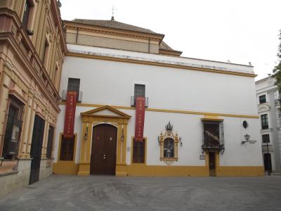 A white and yellow building facade with two red vertical banners reading "2013 AÑO JUBILAR MUSEO" and "2014 AÑO JUBILAR MUSEO", a central arched wooden door, a religious niche with a statue, and a plaque on the right wall that appears to read "PLAZA 