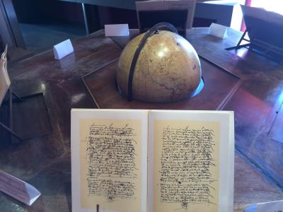 An open historical manuscript with cursive handwriting and a terrestrial globe on a wooden display table inside a museum.