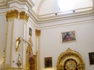 The interior of a church featuring white walls, ornate gold altarpieces, religious paintings, and a high arched ceiling with a flag hanging near the dome.