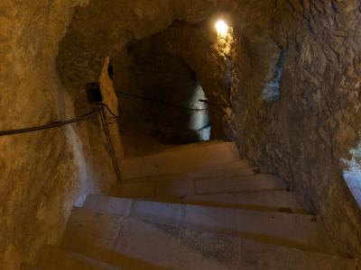A view looking down a stone staircase inside a rough-hewn rock tunnel or cave, illuminated by artificial lighting.
