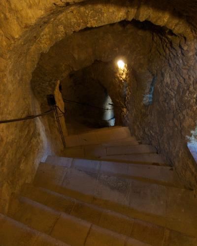 A view looking down a stone staircase inside a rough-hewn rock tunnel or cave, illuminated by artificial lighting.