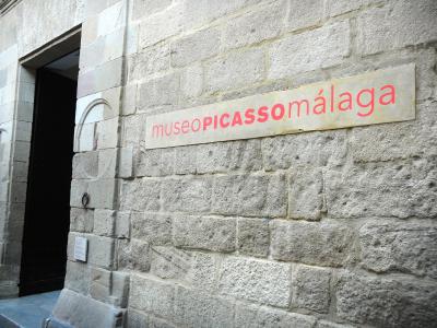 A close-up of a stone building facade featuring a rectangular sign with red text reading "museoPICASSOmálaga" next to a dark doorway.