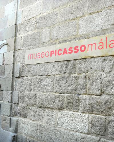 A close-up of a stone building facade featuring a rectangular sign with red text reading "museoPICASSOmálaga" next to a dark doorway.