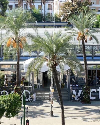A modern, glass-roofed market building with outdoor seating, palm trees, and large white letters spelling "mercado victoria" on the ground in front.